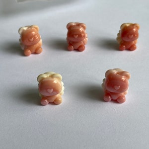 Puede incluir: Cinco pequeñas figuritas de cerámica rosa y blanca con forma de animal. Las figuritas tienen una cara en forma de corazón y están de pie sobre una superficie blanca.