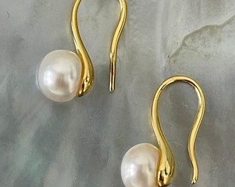 May include: A pair of gold-toned earrings with a single pearl on each earring. The earrings have a simple, elegant design.