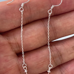 May include: A pair of silver earring findings with a chain and a small loop at the bottom. The findings are designed to be used with a pearl or other bead.