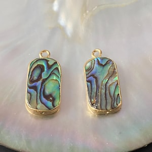 Peut inclure: Deux pendentifs rectangulaires dorés avec des incrustations de nacre d'ormeau. La nacre présente un motif iridescent vert, bleu et violet.