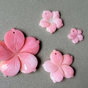 Op de afbeelding: Vier roze bloemvormige hangers in verschillende maten, elk met vijf uitgesneden bloemblaadjes en een klein gaatje aan de bovenkant om op te hangen. De bloemblaadjes hebben een verloop van licht naar donkerroze met een gladde afwerking.