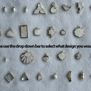 Può includere: Una collezione di ciondoli bianchi e dorati in varie forme, tra cui conchiglie, pesci e disegni geometrici. I ciondoli sono disposti su una superficie bianca. Il testo sull'immagine recita: "Please use the drop down bar to select what design you would like."