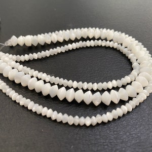 May include: A strand of white moonstone beads with a faceted, teardrop shape. The beads are strung on a clear thread and are arranged in a loose, flowing pattern.