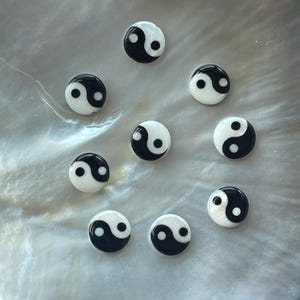 Peut inclure: Dix petits symboles yin yang ronds, blancs et noirs sur une surface blanche nacrée.