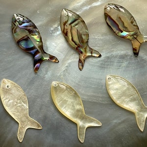 Może przedstawiać: Sześć iryzujących zawieszek w kształcie ryb, trzy z perłowo-białym wykończeniem i trzy z wielokolorowym iryzującym wykończeniem.