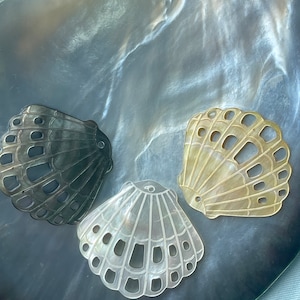 Peut inclure: Trois coquillages décoratifs avec un motif découpé. Les coquillages sont dans des tons de blanc, noir et beige. Les coquillages sont présentés sur une surface en nacre.