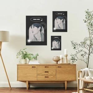 Peut inclure: Trois affiches rectangulaires noires présentant le portrait d'une personne dans un cadre en arc, avec le texte BANG CHAN, des étoiles et des graphiques circulaires. Les affiches sont disposées en différentes tailles sur un mur au-dessus d'un meuble.