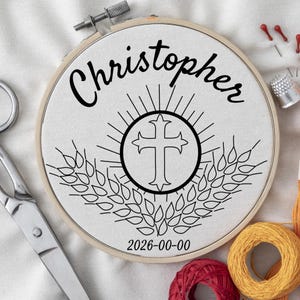 Pode incluir: Um bastidor de bordado circular de madeira contendo tecido branco com um desenho bordado em preto. O design apresenta o nome Christopher, uma cruz central com linhas radiantes, espigas de trigo e a data 2026-00-00 em fio preto.