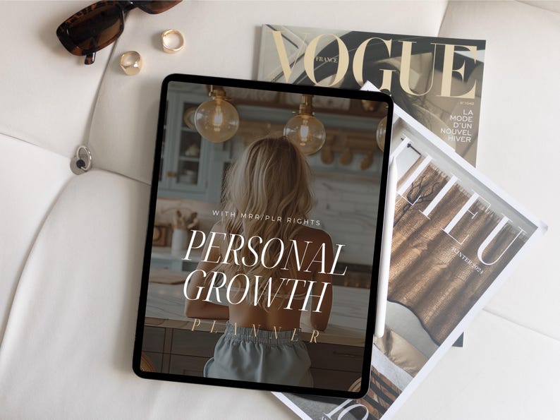 May include: A digital tablet displaying a personal growth planner with the text "WITH MAR/PLA RIGHTS PERSONAL GROWTH PLANNER". The tablet is on a white surface with a magazine and sunglasses.