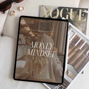 May include: A digital tablet displaying a planner with the text "Money Mindset Planner" and the words "With Marie/PLR Rights" on a white background. The tablet is on top of a white surface with a magazine and a stylus.