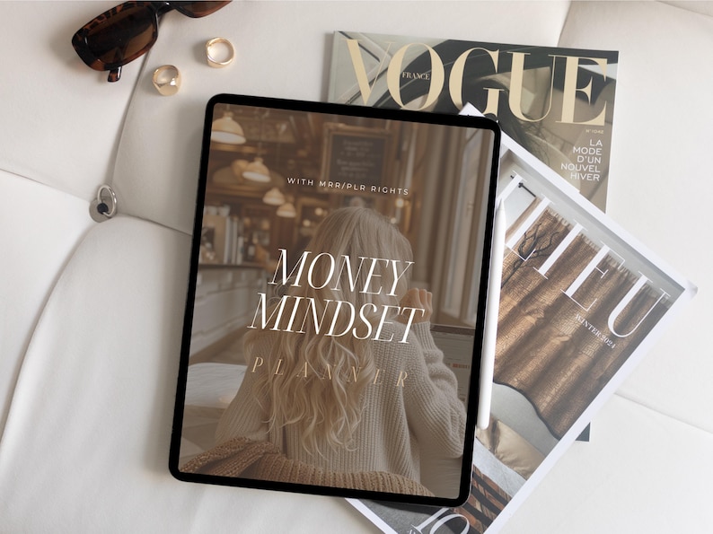 May include: A digital tablet displaying a planner with the text "Money Mindset Planner" and the words "With Marie/PLR Rights" on a white background. The tablet is on top of a white surface with a magazine and a stylus.