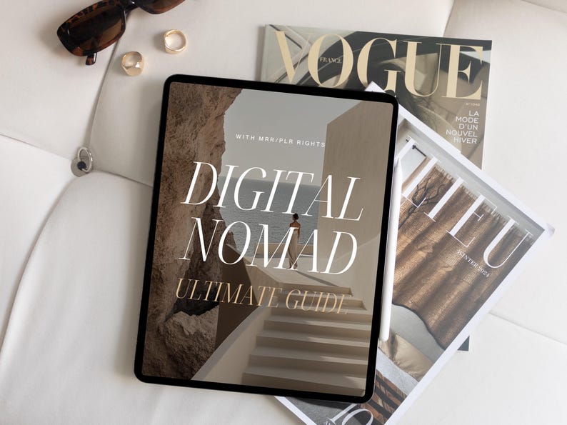 May include: A digital tablet displaying a guide titled "Digital Nomad Ultimate Guide" with a woman walking on a path in the background. The tablet is on a white surface with a magazine titled "Vogue" and another magazine titled "Lieu" visible in the background.