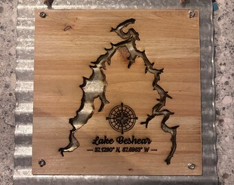 Puede incluir: Un letrero de madera con marco de metal que presenta un contorno quemado del lago Beshear, una brújula y las coordenadas 37.1290° N, 87.6965° W.