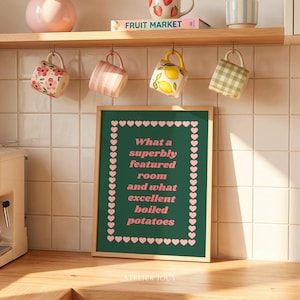 May include: A framed green chalkboard with pink hearts and the text "What a superbly featured room and what excellent boiled potatoes" sits on a wooden surface. Decorative mugs and a book are hanging above.