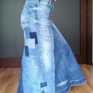 Puede incluir: Falda larga de mezclilla con detalles de patchwork y diseño desgastado. La falda se combina con un top rojo floral y botas negras. La falda es larga hasta el suelo y la mezclilla tiene un lavado azul claro.