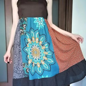 May include: A patchwork dress with a brown bodice and a colorful skirt. The skirt features panels of teal with a floral design, rust with white polka dots, and gray with a paisley pattern. The hemline is black with small white dots.