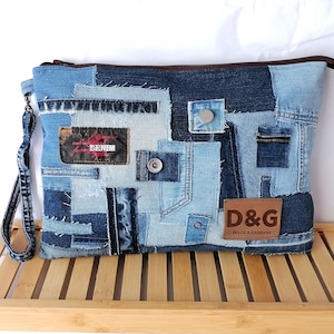 Puede incluir: Una cartera de mano de mezclilla azul con una cremallera de cuero marrón y un parche de cuero marrón que dice "D&G DOLCE & GABBANA". La bolsa está hecha de mezclilla de retazos y tiene una correa larga de mezclilla.