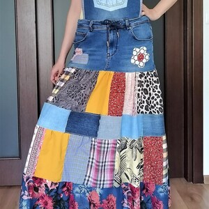 Puede incluir: Vestido patchwork de mezclilla con peto y falda larga. La falda presenta una variedad de patrones de tela, incluyendo estampados florales, de leopardo y a cuadros. El vestido tiene tirantes ajustables y cintura con cordón. Se ve una camiseta amarilla debajo.