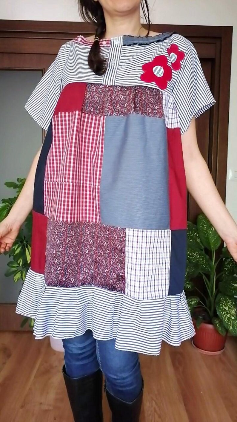 May include: A patchwork dress in red, blue, and white, with short sleeves and a ruffled hem. The dress incorporates striped, checked, and floral patterned fabrics. It features a red flower applique. The dress is a unique, handcrafted design.