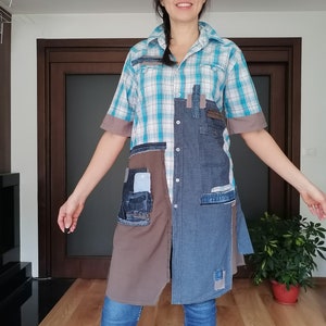 May include: A patchwork tunic dress featuring a blue and white plaid top, denim and brown fabric panels, and short sleeves. The dress has a collared neckline and pockets, and is worn with blue jeans and boots.