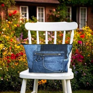 Op de afbeelding: Een blauwe spijkerstof etui met een patchworkontwerp van verschillende tinten denim. De voorkant van de etui is voorzien van een functioneel vak met een metalen ritssluiting en een zichtbare naad van een broekzak.