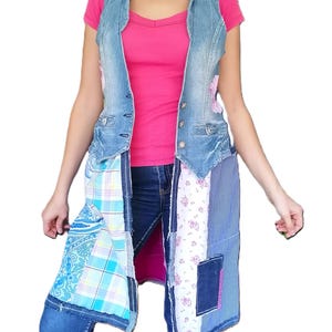 Op de afbeelding: Een lang mouwloos vest met een lichtblauw spijkerstof lijfje met zilveren knopen en een onderkant opgebouwd uit diverse stoffen lappen, waaronder blauw paisley, ruitjespatroon, witte bloemenprint en donkerblauwe spijkerstof vierkanten.