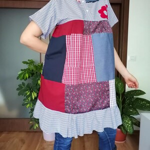 May include: A patchwork dress in red, blue, and white fabrics. The dress has short sleeves, a ruffled hem, and a red flower applique. The top is striped, and the bottom is a mix of patterns. The dress is knee-length.