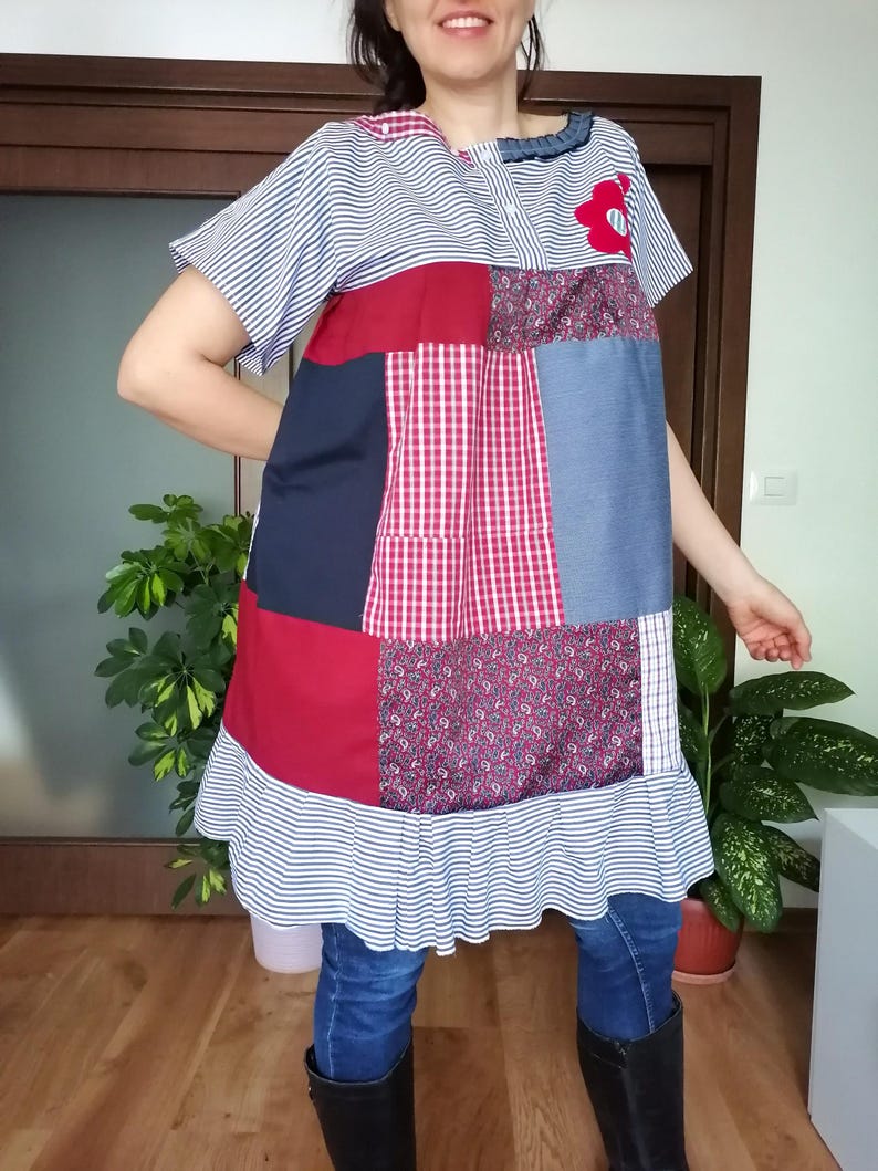 May include: A patchwork dress in red, blue, and white fabrics. The dress has short sleeves, a ruffled hem, and a red flower applique. The top is striped, and the bottom is a mix of patterns. The dress is knee-length.