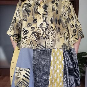 May include: A patchwork shirt and skirt combination. The top is yellow with black leaf and geometric patterns. The skirt features a mix of grey, yellow, and black fabrics with diverse designs, including polka dots and geometric shapes. A pocket is visible on the skirt.