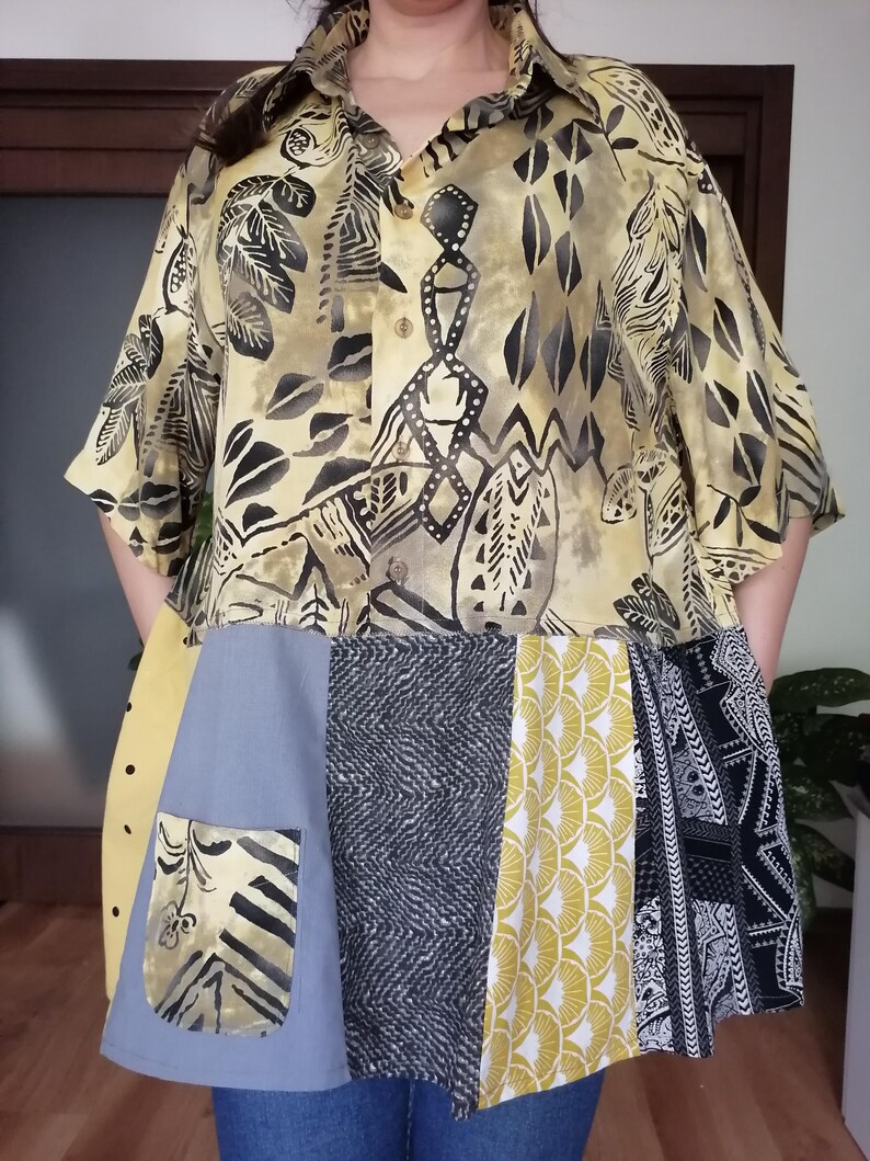 May include: A patchwork shirt and skirt combination. The top is yellow with black leaf and geometric patterns. The skirt features a mix of grey, yellow, and black fabrics with diverse designs, including polka dots and geometric shapes. A pocket is visible on the skirt.