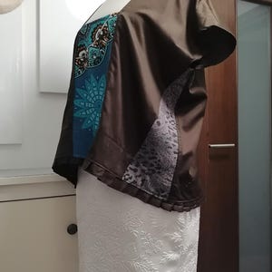 May include: A brown, short-sleeved top with a square neckline. The top features a teal and black patterned panel, a gray animal print panel, and a white floral skirt. The garment is displayed on a mannequin.