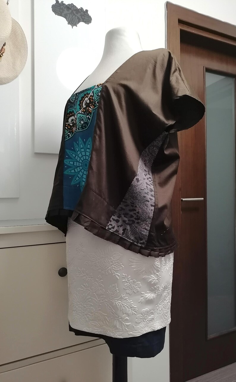 May include: A brown, short-sleeved top with a square neckline. The top features a teal and black patterned panel, a gray animal print panel, and a white floral skirt. The garment is displayed on a mannequin.