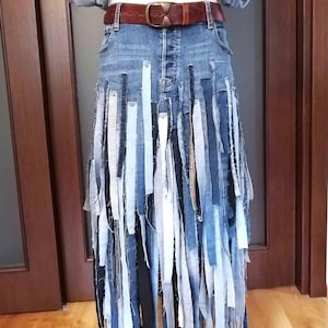 May include: A denim skirt with vertical strips of varying denim shades, creating a fringed effect. The skirt is paired with a brown leather belt and a denim jacket. The skirt's length is 37 inches at the ankle.