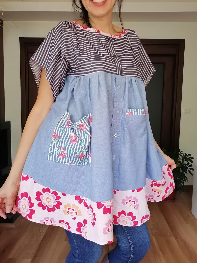 May include: A patchwork tunic dress with a striped top, light blue denim-style fabric, and floral details. The dress has a pink floral hem and pocket details. It features short sleeves and a button-down front.