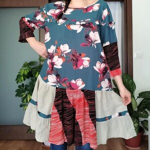 Peut inclure: Robe turquoise ornée de fleurs blanches et roses. Les manches présentent un motif rayé noir et rouge. La jupe est un patchwork de panneaux rouges, noirs et beiges. La robe est de longueur genou.