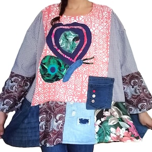 Könnte beinhalten: Ein Patchwork-Tunika-Top mit einem Schmetterlingsdesign. Das Oberteil kombiniert rosa geometrische, blau-karierte und florale Muster. Jeans-Taschen und -Patches sorgen für Textur. Die Ärmel haben einen Paisley-Druck.