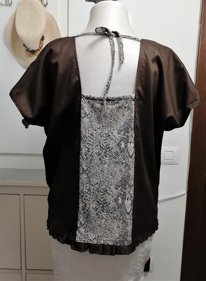May include: A brown satin top with short sleeves and a square neckline. The back features a panel of grey and white snakeskin print fabric. The top is displayed on a mannequin.