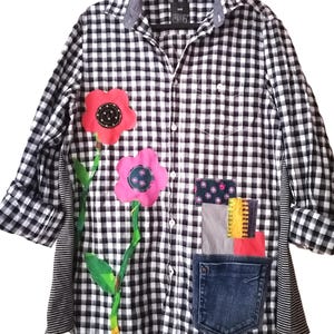 May include: Black and white checkered button-down shirt with floral and patchwork embellishments. Features two large pink flowers with green stems and leaves, a denim pocket, and various fabric patches.
