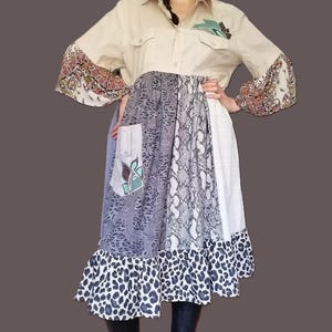 Puede incluir: Vestido camisero beige con estampados mixtos. La parte superior es una camisa abotonada con un diseño de hojas. La falda presenta paneles con estampado de cachemira, piel de serpiente y leopardo. Las mangas tienen un estampado de cachemira y el vestido tiene un dobladillo con volantes.