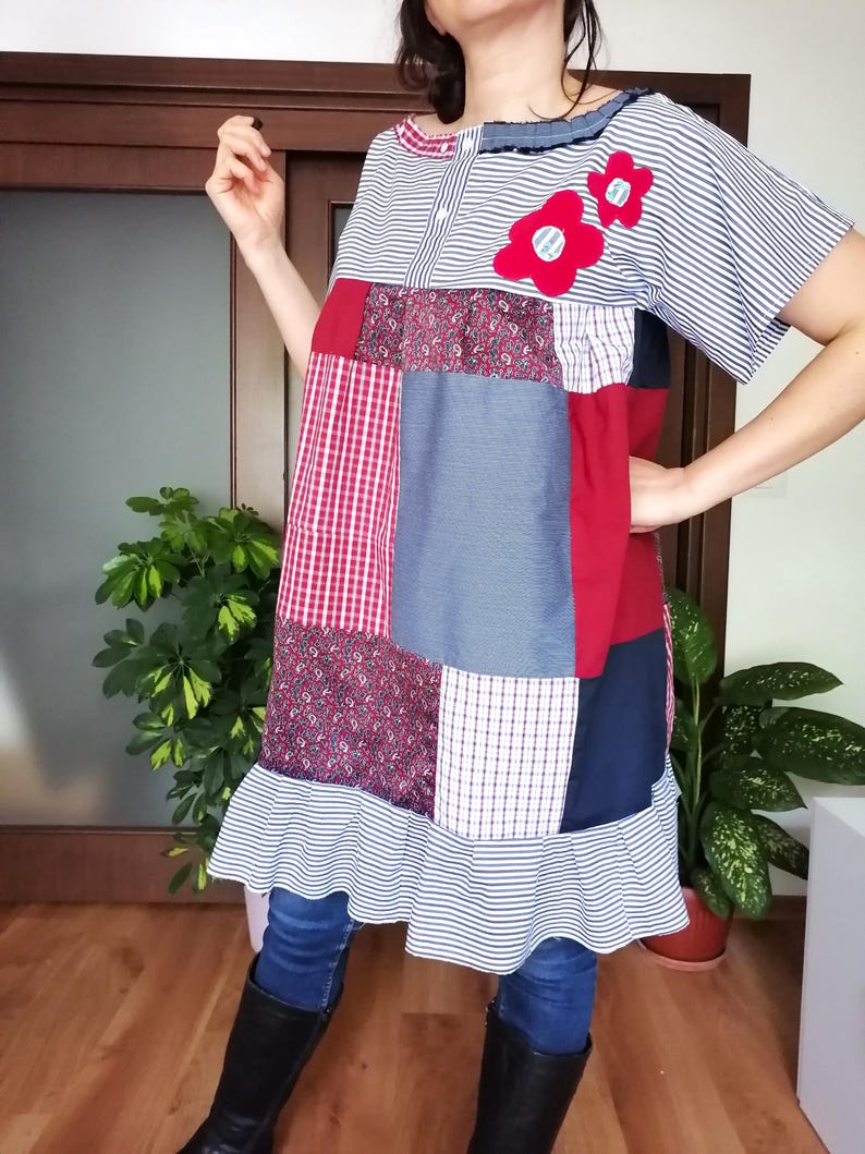 May include: A patchwork dress with a variety of patterns and fabrics, such as stripes, checks, and floral designs. The dress has short sleeves, a frilled hem, and is decorated with two red flower appliqu&eacute;s. The colour scheme includes red, white, blue, and navy.