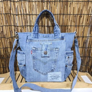 May include: Light blue denim tote bag with two handles and a detachable shoulder strap. Features a front pocket with a button closure and two side pockets. Includes a Levi Strauss & Co. label.