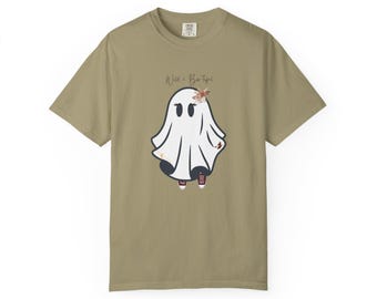 May include: Olive green t-shirt featuring a cartoon ghost with a floral headpiece and red sneakers. The ghost has black eyes and is wearing a white sheet. The text "Wild & Beautiful" is above the ghost.
