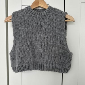 Könnte beinhalten: Eine graue, ärmellose Strickweste mit Rundhalsausschnitt.