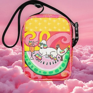 May include: A colorful crossbody bag with a whimsical design. The bag features a poodle wearing sunglasses and a chicken on a watermelon slice, with a cocktail. The bag has a black strap and a pink, yellow, and red color scheme.