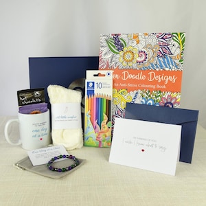 May include: A gift set containing a white mug with the text one day at a time, a pair of cream-coloured fuzzy socks, a pack of 10 coloured pencils, a Garden Doodle Designs colouring book, a beaded bracelet, and a card reading I wish I knew what to say.