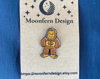 Bigfoot Enamel Pin with Heart Hands, Cute Cryptid Gift, Sasquatch Lapel Pin for Backpacks, Paranormal Collector Flair, Spooky Cute Pin