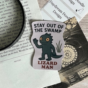 May include: A sticker with a cartoon lizard wearing a white shirt and the text "Stay Out of the Swamp" and "Lizard Man".