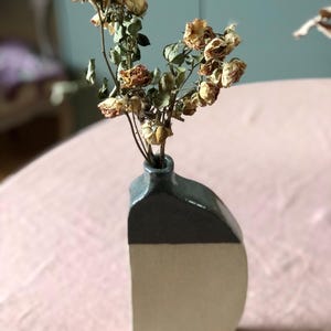 Peut inclure: Un vase en céramique avec un dessus gris et un fond blanc. Le vase est rempli de roses séchées.