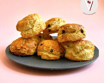Puede incluir: Una pila de scones dorados con chispas de chocolate sobre un plato gris oscuro. Los productos horneados están dispuestos sobre un fondo rosa pálido. La imagen incluye un logotipo que dice "Veg'n'Licious Vegan Patisserie."