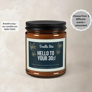 Peut inclure: Une bougie en pot de verre marron avec un couvercle noir. L'étiquette indique "Smells like HELLO TO YOUR 30s!" avec du texte indiquant que les bougies sont non toxiques et disponibles en 5 parfums. La bougie est coulée à la main aux États-Unis.